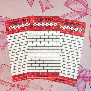 May include: Three cards with a brick wall design. The top section is red with the text "COLOUR THE BRICKS" and circles with monetary values in pounds. The brick section is white with black outlines. The cards are on a pink background.