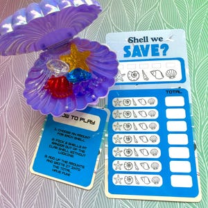 May include: A purple iridescent plastic clam shell container holding small translucent plastic sea creatures in yellow, blue, and red. Included are two blue game cards with white text reading Shell we SAVE? and HOW TO PLAY, featuring rows of shell icons and blank spaces for tracking totals.