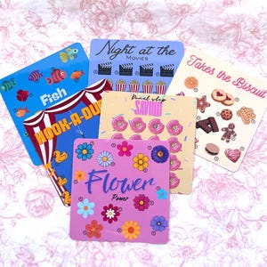 May include: A selection of square cards with bright designs and text. One card shows fish and the text "Fish Hook-A-Duck". Another says "Night at the Movies". Other cards feature donuts, flowers, and biscuits.