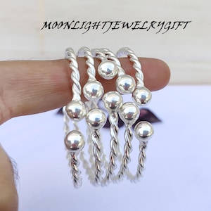 Può includere: Anelli color argento con un design a fascia intrecciata e una piccola sfera sulla parte superiore. Gli anelli sono esposti su un dito. Il testo "MOONLIGHTJEWELRYGIFT" è nella parte superiore dell'immagine.