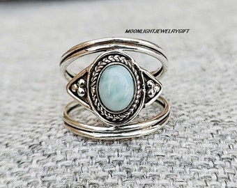 Può includere: Un anello d'argento con una pietra ovale blu chiaro incastonata in una lunetta decorativa. L'anello ha un design a doppia fascia.