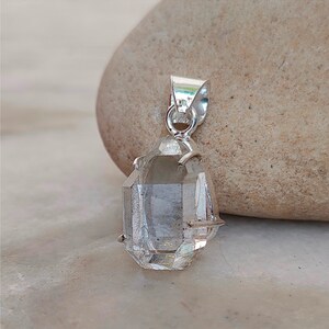 May include: A clear quartz crystal pendant with a silver setting. The crystal is faceted and has a teardrop shape.
