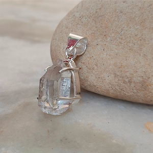 May include: A clear quartz crystal pendant with a silver setting. The crystal is faceted and has a natural, raw look. The pendant is perfect for adding a touch of natural beauty to any outfit.