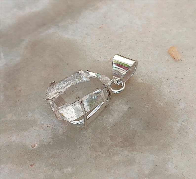 May include: A clear quartz crystal pendant with a silver bail. The crystal is faceted and has a natural, rough appearance.