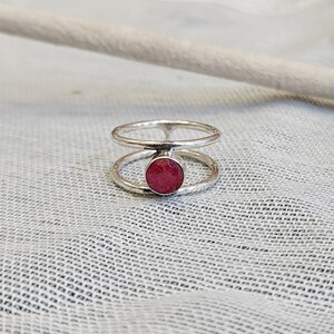 Może przedstawiać: Srebrny pierścionek z podw&oacute;jną obręczą i okrągłym, r&oacute;żowym kamieniem szlachetnym w środku.