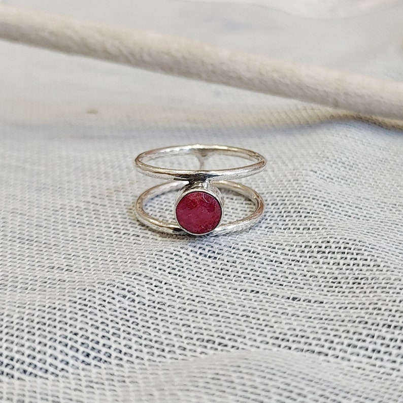 Może przedstawiać: Srebrny pierścionek z podw&oacute;jną obręczą i okrągłym, r&oacute;żowym kamieniem szlachetnym w środku.