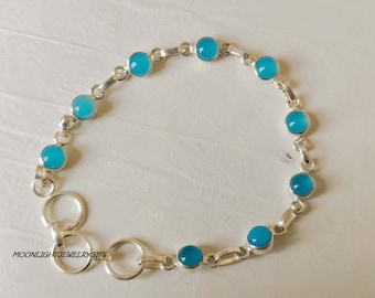 May include: A silver bracelet with light blue gemstones. The bracelet has a series of links and gemstones, with a clasp. The bracelet is displayed on a white surface. The gemstones are a vibrant shade of blue.