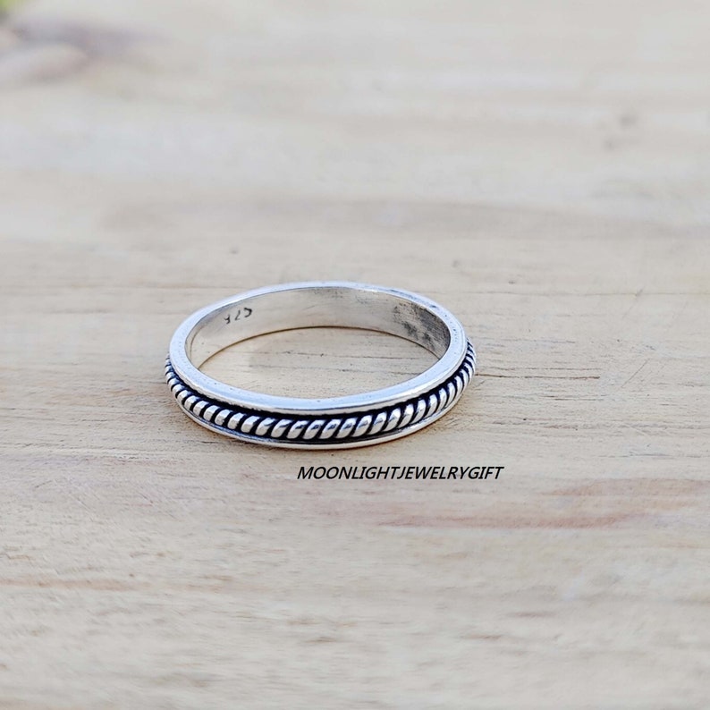 May include: A silver ring with a rope-like design around the band.