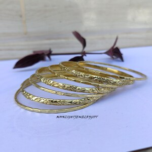 以下が含まれることがあります： 花柄の金色のバングル6個セット。バングルは重ねてあります。