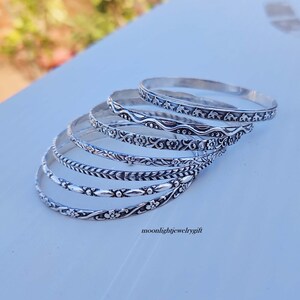 Pu&ograve; includere: Un set di sei braccialetti d'argento con diversi disegni in rilievo. I braccialetti sono impilati uno sopra l'altro, con il braccialetto superiore che presenta un design a delfino.