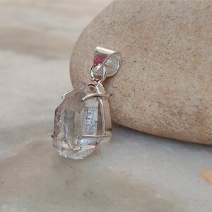 May include: A clear quartz crystal pendant with a silver setting. The crystal is faceted and has a natural, raw look. The pendant is perfect for adding a touch of nature to any outfit.