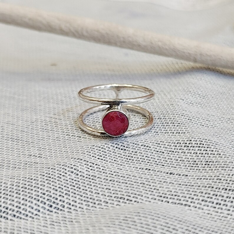 Może przedstawiać: Srebrny pierścionek z podw&oacute;jną obręczą i okrągłym, r&oacute;żowym kamieniem szlachetnym w środku.