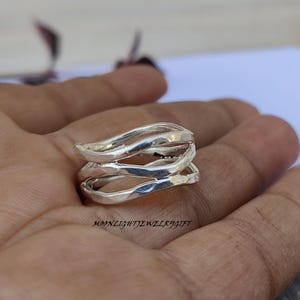 May include: A silver ring with a wavy, organic design. The ring is made of three bands that are intertwined and have a hammered finish.
