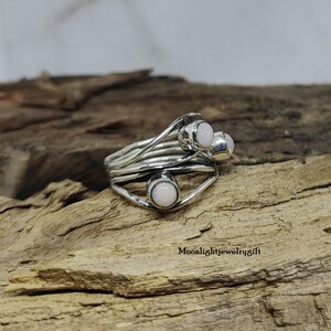 Pu&ograve; includere: Un anello d'argento con tre pietre di opale bianco incastonate in un design a filo ritorto.
