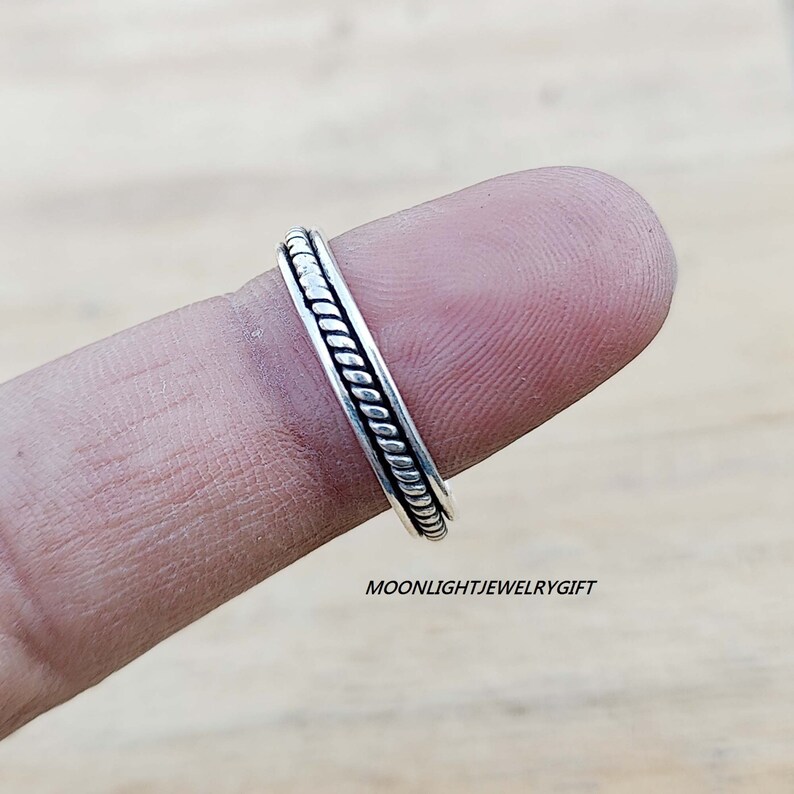 May include: A silver ring with a braided design. The ring is on a finger.