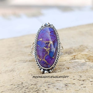 May include: A silver ring with an oval-shaped purple and gold gemstone. The ring has a rope-like design around the edge of the setting.