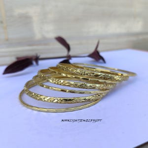 以下が含まれることがあります： 花柄の金色のバングル6個セット。バングルは重ねてあります。