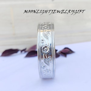 Pode incluir: Um bracelete de prata com um design floral. O bracelete é liso e brilhante.