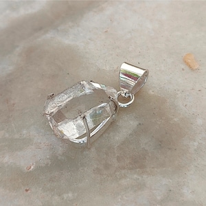 May include: A clear quartz crystal pendant with a silver setting. The crystal is faceted and has a natural, rough appearance. The pendant is attached to a silver bail.