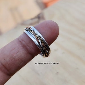 Pu&ograve; includere: Un anello girevole in argento, rame e oro. L'anello &egrave; composto da tre bande intrecciate. L'anello viene indossato su un dito.