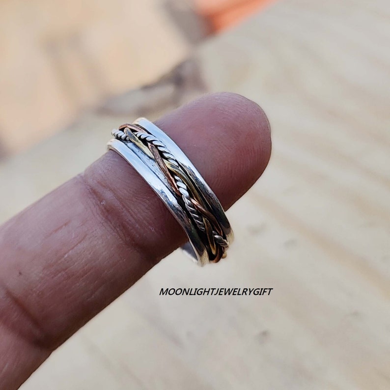 Pu&ograve; includere: Un anello girevole in argento, rame e oro. L'anello &egrave; composto da tre bande intrecciate. L'anello viene indossato su un dito.