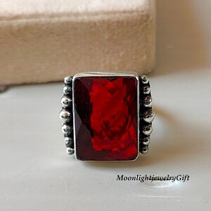 Puede incluir: Un anillo de plata con una gran piedra preciosa roja rectangular engastada en un engaste de cuentas.