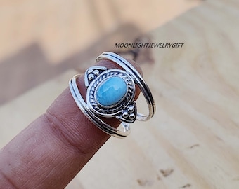 Può includere: Un anello d'argento con una pietra ovale blu chiaro incastonata in una montatura in argento decorata. L'anello ha un design a doppia fascia.
