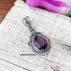 May include: A silver pendant featuring a pear-shaped, faceted purple gemstone set in an ornate metal frame with intricate scrollwork, beaded edges, and a twisted rope border. The text MOONLIGHTJEWELRYGIFT is printed in black on the surface below.