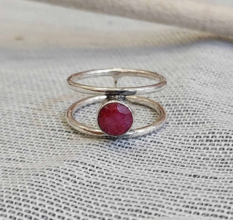 Może przedstawiać: Srebrny pierścionek z podw&oacute;jnym obrączką i czerwonym kamieniem szlachetnym w środku.