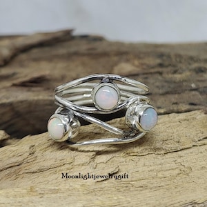 Pu&ograve; includere: Un anello d'argento con tre pietre di opale bianco incastonate in un design a filo ritorto.