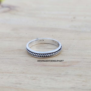 May include: A silver band ring with a rope-like design around the edge. The ring is marked with the number "925" on the inside.