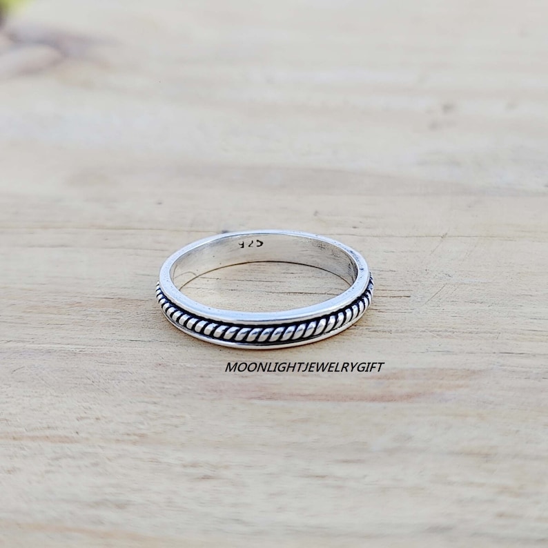 May include: A silver band ring with a rope-like design around the edge. The ring is marked with the number "925" on the inside.