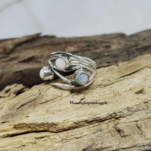 Pu&ograve; includere: Un anello d'argento con tre pietre di opale incastonate in un design a filo ritorto.