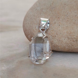 May include: A clear quartz crystal pendant with a silver setting. The crystal is faceted and has a teardrop shape.