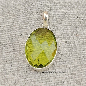 May include: A silver pendant featuring a large, faceted, oval-shaped green gemstone.