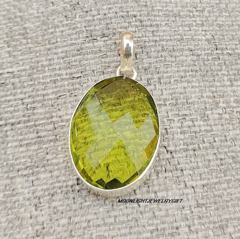 May include: A silver pendant featuring a large, faceted, oval-shaped green gemstone.