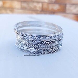 Pu&ograve; includere: Un set di sei braccialetti d'argento con disegni intricati. I braccialetti presentano una variet&agrave; di motivi, tra cui onde, foglie e fiori. I braccialetti sono impilati uno sopra l'altro, creando un look a strati.