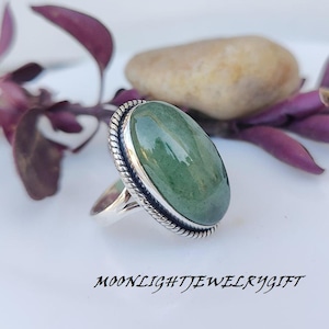 Puede incluir: Un anillo de plata con una piedra ovalada verde engastada en un engaste de plata. El anillo tiene un diseño de cuerda alrededor del engaste.