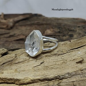 May include: A silver ring with a clear quartz crystal set in the center. The ring is on a wooden surface.