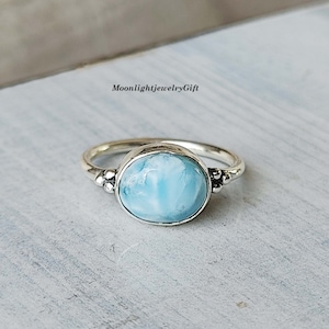 May include: A silver ring with a light blue oval-shaped gemstone. The ring has small silver beads on each side of the stone.