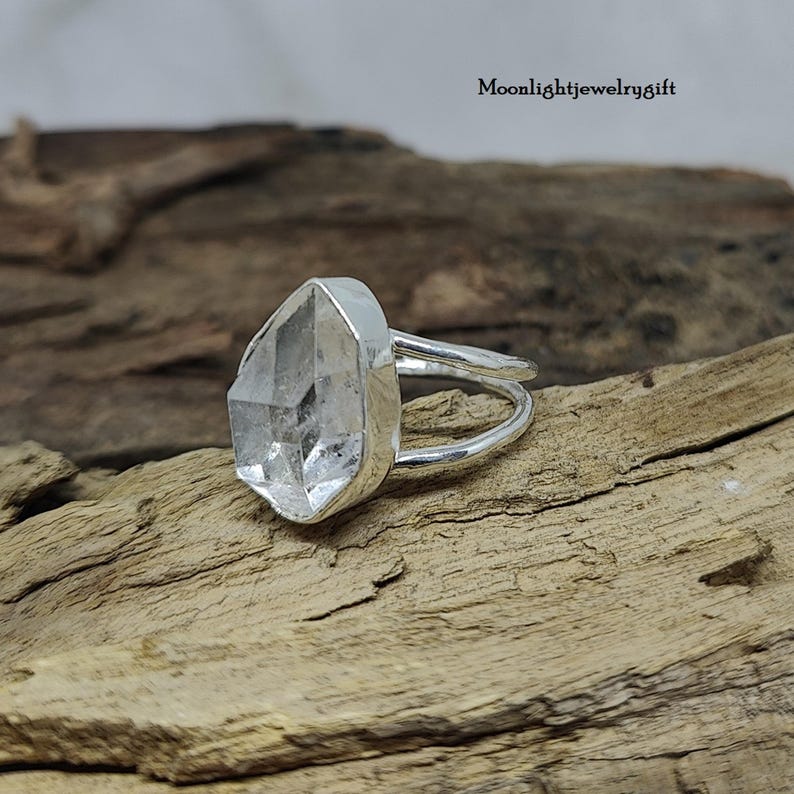 May include: A silver ring with a clear quartz crystal set in the center. The ring is on a wooden surface.