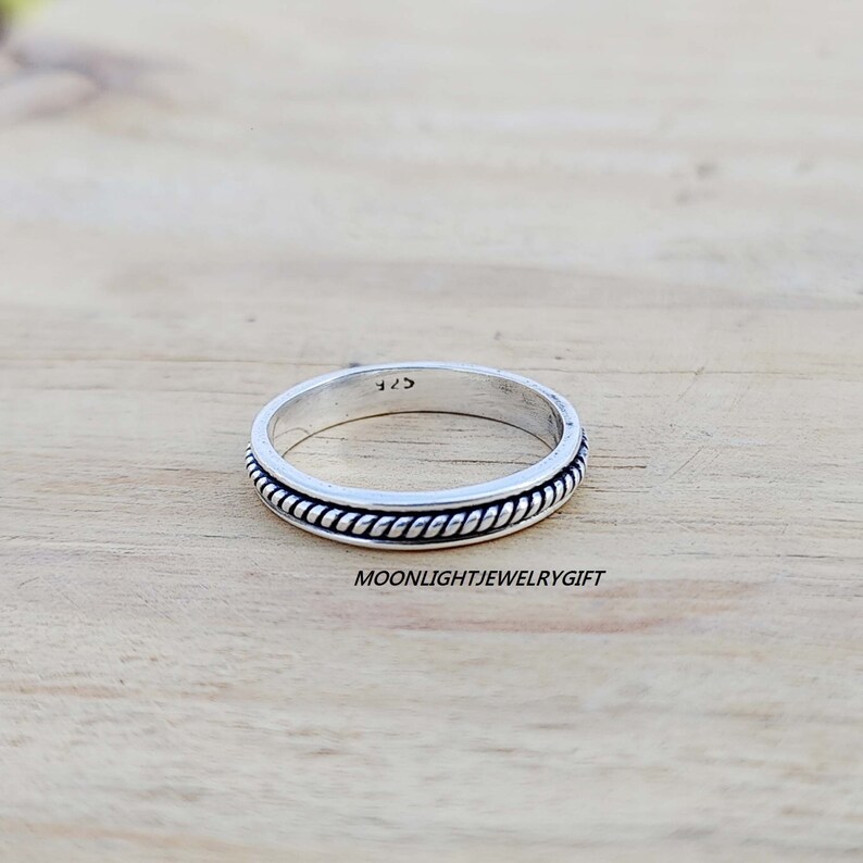 May include: A silver band ring with a rope-like design around the edge. The ring is marked with the number "925" on the inside.