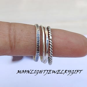 Puede incluir: Conjunto de cuatro anillos apilables de plata. Los anillos son de diferentes estilos, incluyendo una banda texturizada, una banda lisa y una banda trenzada.
