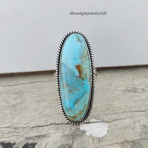 May include: A silver ring with a large oval turquoise stone. The stone has a blue and green color with brown veins.
