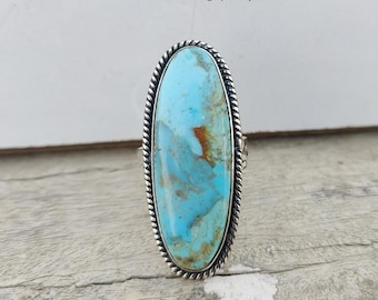 Può includere: Un anello d'argento con una grande pietra ovale di turchese. La pietra ha un colore blu e verde con venature marroni.