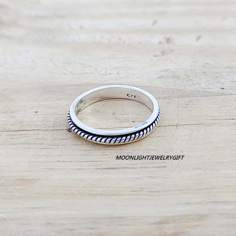 May include: A silver ring with a rope design around the band. The ring is on a wooden surface.