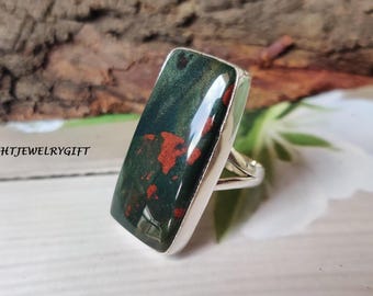 May include: A rectangular ring featuring a large, polished gemstone with a dark green base and red inclusions. The stone is set in a silver band. The text "HTJEWELRYGIFT" is visible in the image.