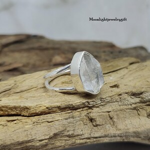 May include: A silver ring with a clear quartz crystal set in a bezel setting. The ring is made of sterling silver and has a simple, elegant design.
