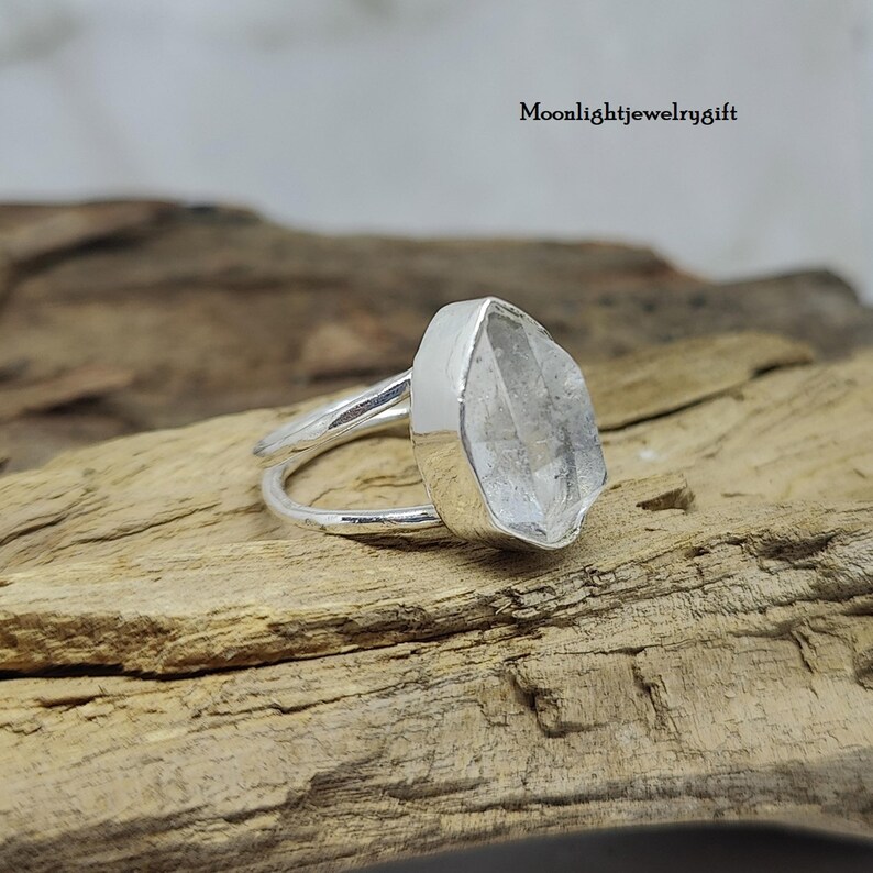 May include: A silver ring with a clear quartz crystal set in a bezel setting. The ring is made of sterling silver and has a simple, elegant design.