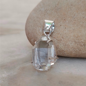 May include: A clear quartz crystal pendant with a silver setting. The crystal is faceted and has a teardrop shape.